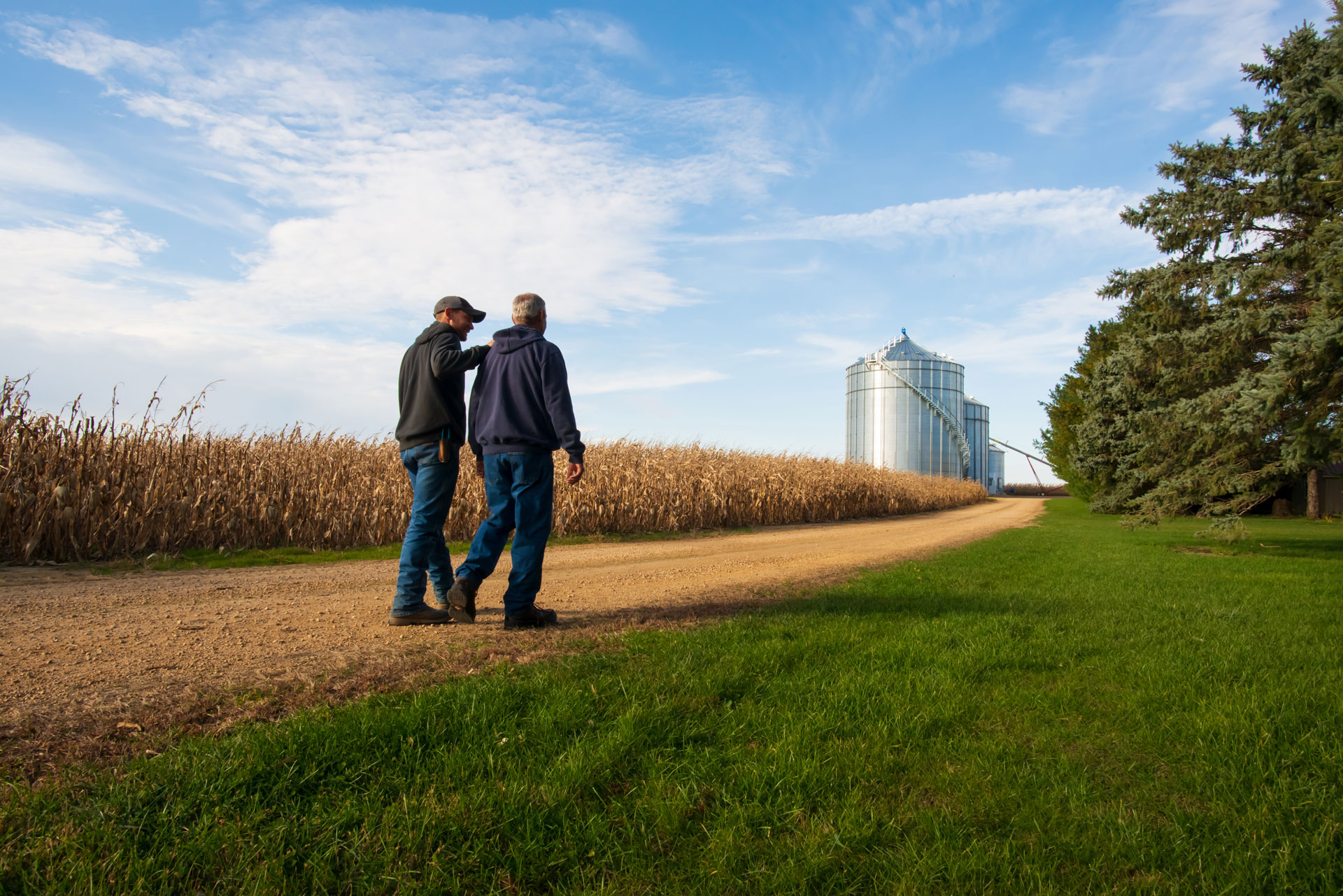 two farmers walking past a field towards grain bins | Shivvers